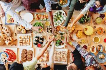 A diverse group of people, including men and women of various ethnicities, joyfully sharing a feast. The table is filled with delicious food, showcasing a vibrant and communal dining experience.
