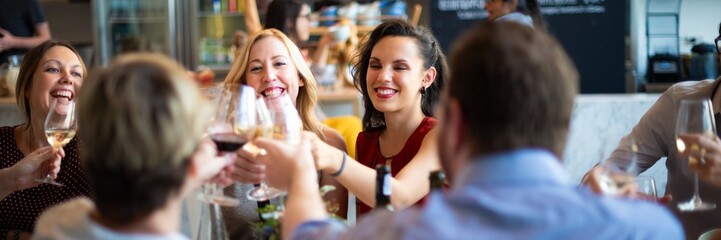 Group of people toasting with wine glasses at a restaurant. Smiling friends enjoying a meal....