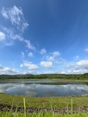 Calm reservoir water reflecting blue skies and distant hills on a bright tropical morning.