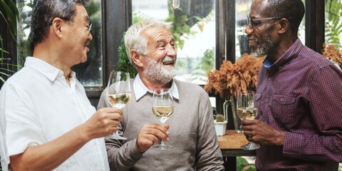 Three elderly diverse men enjoying wine together, smiling and chatting. Diverse group of man friends, sharing laughter and drinks in a cozy restaurant. Diverse old men talking together in restaurant.