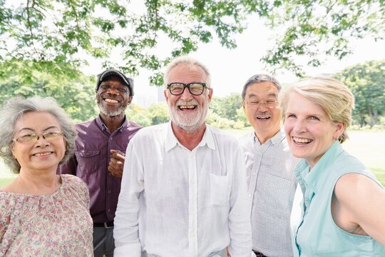 Group of diverse elderly friends smiling outdoors. Elderly men and women enjoying nature. Happy elderly group in a park setting, sharing joy and laughter. Happy diverse retired old people smiling.