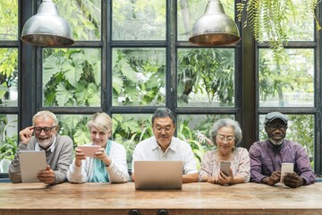 Diverse group of seniors using devices. Elderly men and women with tablets and laptops. Multicultural seniors enjoying technology together indoors. Senior people using digital devices and social media