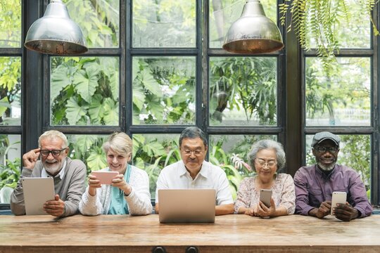 Diverse group of seniors using devices. Elderly men and women with tablets and laptops. Multicultural seniors enjoying technology together indoors. Senior people using digital devices and social media