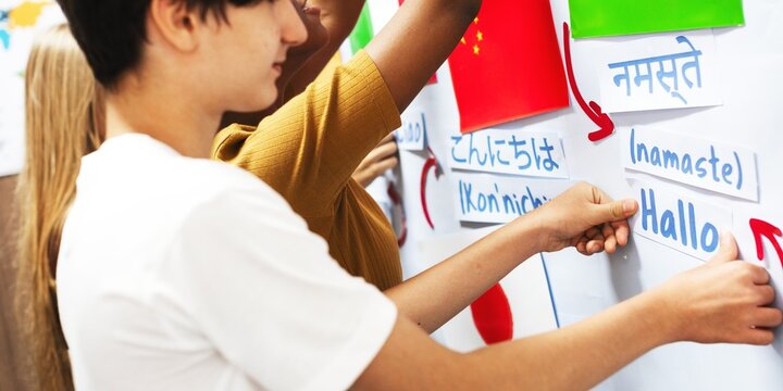 Students placing multilingual greeting cards on a board. Diverse group engaging with language learning. Multilingual interaction with greetings. Students learning in classroom with nation flags.