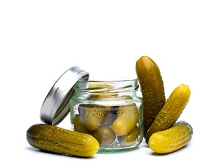 Several green pickled gherkins are arranged around an open glass jar with a metal lid on a clean white background.