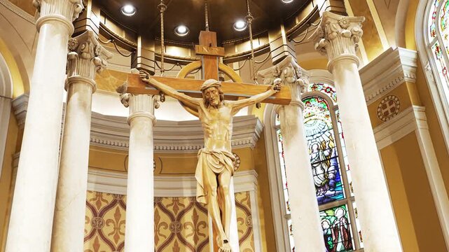 Jesus Christ on wooden crucifix in a cathedral catholic church with bright lights, beautiful columns and stained glass windows.