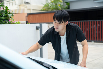 Man cleaning car windshield with cloth outdoors, focused young adult wiping vehicle glass in...