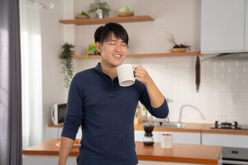 Young man enjoying morning coffee in modern kitchen, smiling with eyes closed, relaxed and content,...