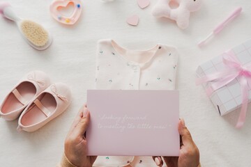 Baby shower invitation with pink baby shoes, a gift box, and a card. Baby clothes and baby-themed...