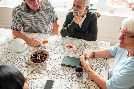 Group of elderly people sitting at a table with tea and fruit, enjoying conversation. Warm, friendly gathering of seniors sharing stories and laughter. Elderly people daily life photo.