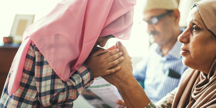 A touching moment between a Muslim girl in a pink hijab and her grandmother. The girl shows affection, highlighting family bonds in a warm, loving atmosphere. This scene captures cultural values.
