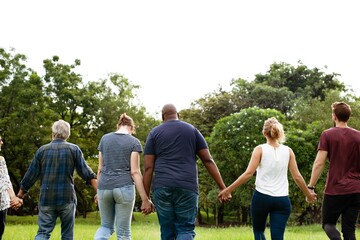 Diverse group of friends hold hands at park. Diverse group of men and women standing together hold hands at park. Group of diverse friends, men and women, standing in hold hands on grass. Back view