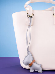 Close-up of a fashionable gray leather bulldog keychain with a collar and a bow, attached to a  white stylish bag