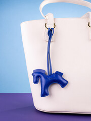 Close-up of a fashionable blue leather horse keychain with a saddle, attached to a white stylish bag