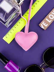 Close-up of a fashionable pink leather heart-shaped keychain on purple table with women accessories