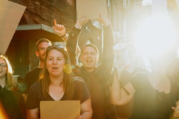 Group of people at a protest, holding signs and a megaphone, with sunlight in the background. Energetic protest scene with diverse participants. Group of diverse people protesting with blank signs.