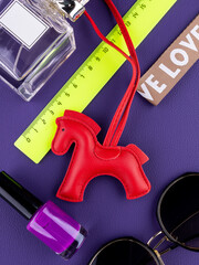 Close-up of a fashionable red leather horse keychain with a saddle on purple table with women accessories