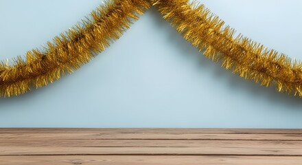 Festive gold tinsel garland on blue wall with wooden surface