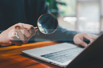 A business person using a magnifying glass near a laptop with a transparent search bar interface, representing online searching, data analysis, investigation, SEO research, and digital information