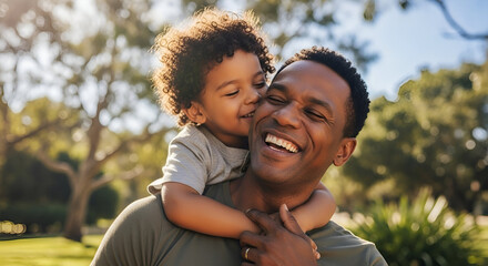 Joyful African American father and son enjoying outdoor park day with smiles and playful embrace on sunny afternoon in lush green setting