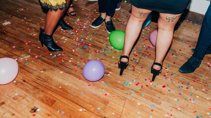 Party scene with colorful balloons and confetti on a wooden floor. People in stylish shoes,...