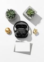 Top-down view of black wireless headphones, succulent plants, golden Christmas ornaments, and a blank card on a white background.