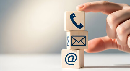 Hand arranging wooden blocks with icons of a phone email and at symbol representing communication methods and digital connectivity in a modern business setting