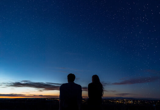 A man and a woman stand together under a beautiful starry night sky