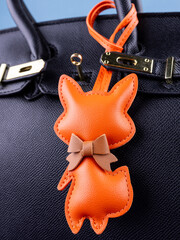 Close-up of a fashionable orange leather fox keychain with a bow, attached to a black stylish bag