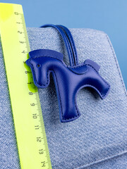 Close-up of a fashionable blue leather horse keychain with a saddle, attached to a blue stylish bag