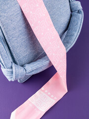Close-up of a pink silk ribbon with a cartoon bunny pattern on a blue leather bag