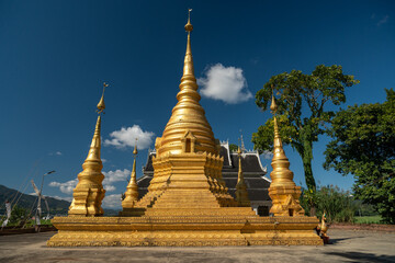 Fototapeta premium Bright Golden Buddhist Stupa and Pagoda Against a Clear Blue Sky