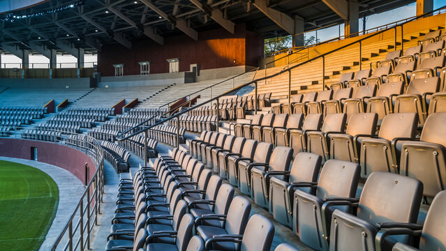 Empty rows of stadium seats bathed in warm sunlight at a large outdoor sports arena.