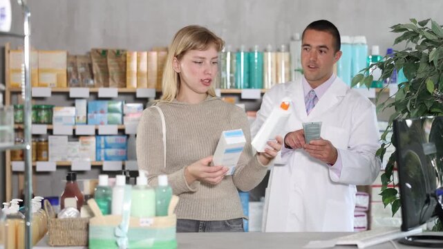 Girl studies composition of body lotion, buys product in drug store. Checking for absence of GMOs, age restrictions and recommendations for use. Man pharmacist in background offers similar product