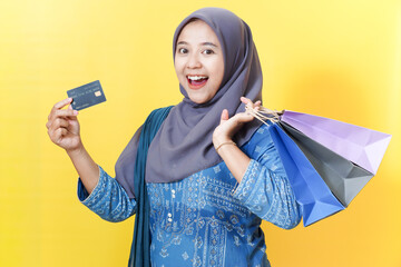 Happy woman in hijab with shopping bags and credit card on yellow background.