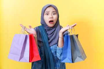 Shocked woman in hijab with shopping bags on yellow background.