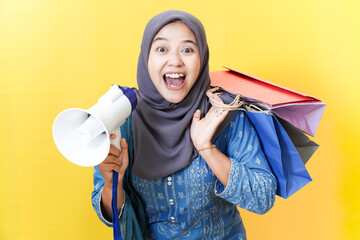 Excited woman with shopping bags and megaphone on yellow background.