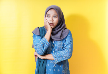 Worried woman in hijab with hand on cheek against yellow background.
