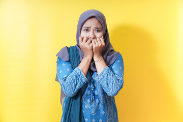 Scared woman in hijab biting nails against yellow background.