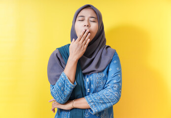 Tired woman in hijab yawning against yellow background.