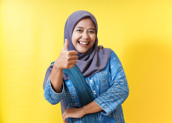 Smiling woman in hijab gives thumbs up on yellow background.