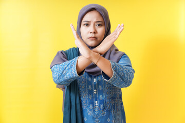 Woman in hijab crosses arms in disapproval on yellow background.