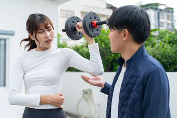 Woman lifting dumbbell with man coaching her during outdoor workout session