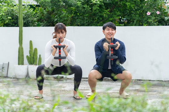 Young couple exercising with dumbbell squat outdoors in garden with green plants