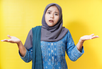 Confused woman in hijab shrugging on yellow background.