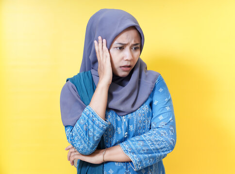Worried woman in hijab with hand on face against yellow background.