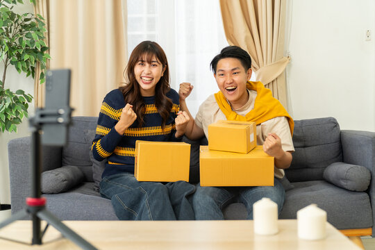 Happy young couple holding cardboard box and celebrating success on sofa - Powered by Adobe