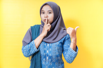 Woman in hijab gesturing silence and pointing right.