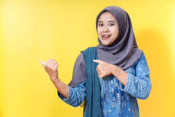 Smiling woman in hijab pointing and gesturing on yellow background.