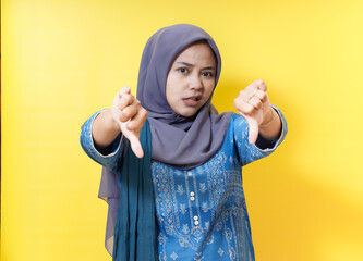 Woman in hijab gives thumbs down on yellow background.